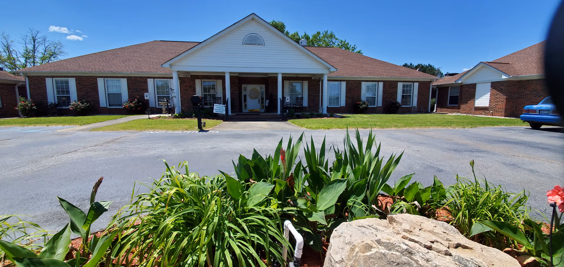 Front exterior of a single-story brick senior living facility with a landscaped entrance.