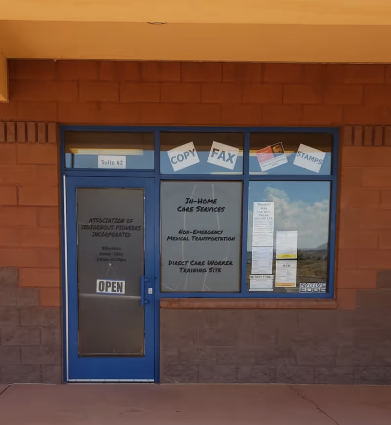 Blue-framed storefront exterior with a door and windows displaying signage for Association of Indigenous Pioneers, Incorporated.