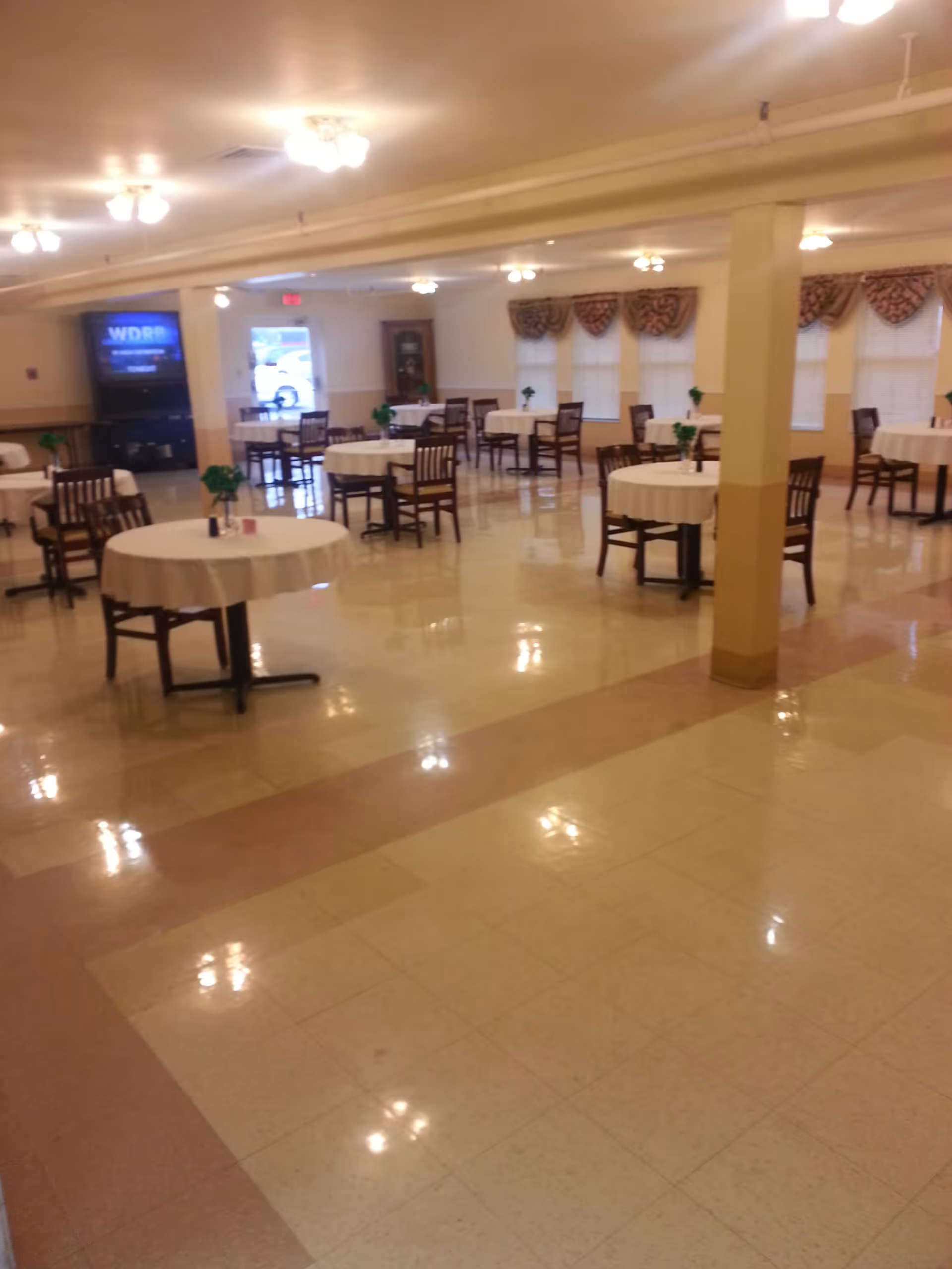 Large dining room with round tables draped in white tablecloths and wooden chairs under ceiling lights.