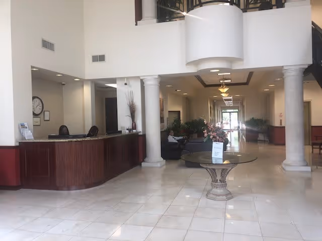 Lobby in a senior living facility with reception desk, seating, columns, and plants.