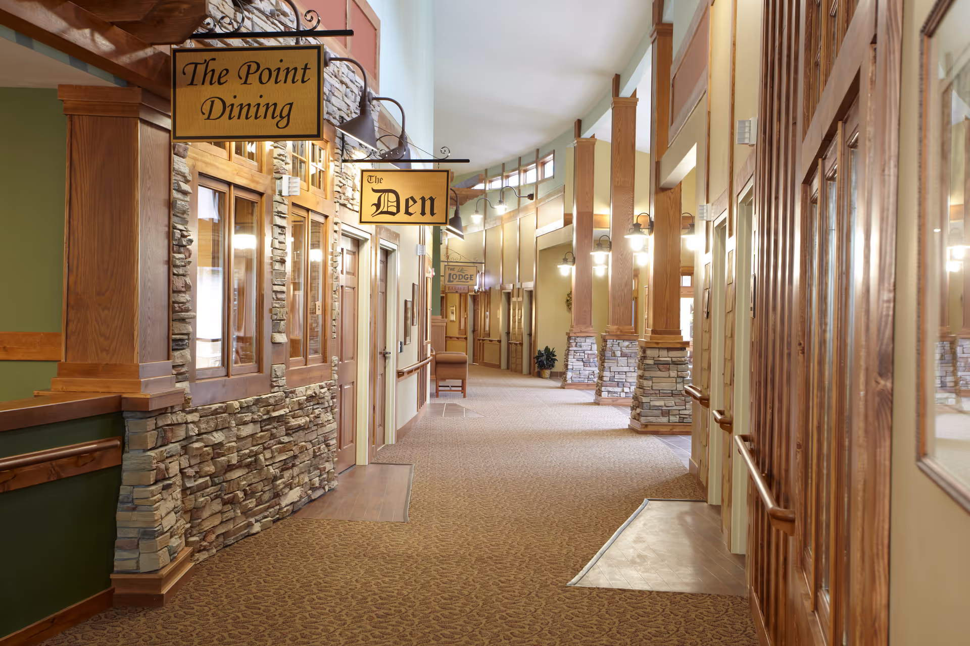 Interior corridor with stone-wrapped walls, wooden columns, and dining and den signs.
