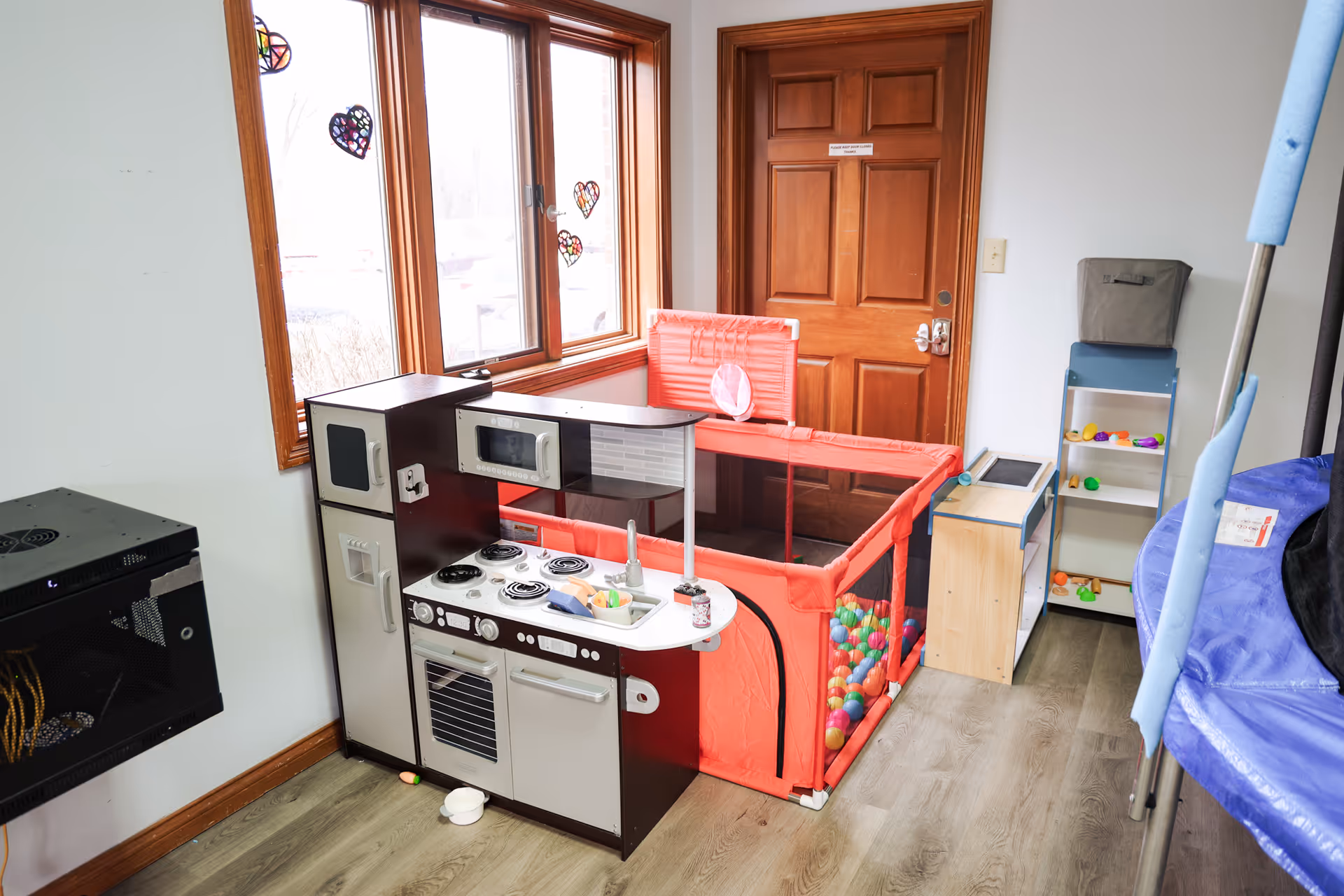 Indoor play area with toy kitchen, red playpen, and shelves by the window