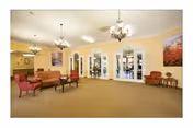 A spacious senior living lounge with yellow walls, chandeliers, and comfortable seating.
