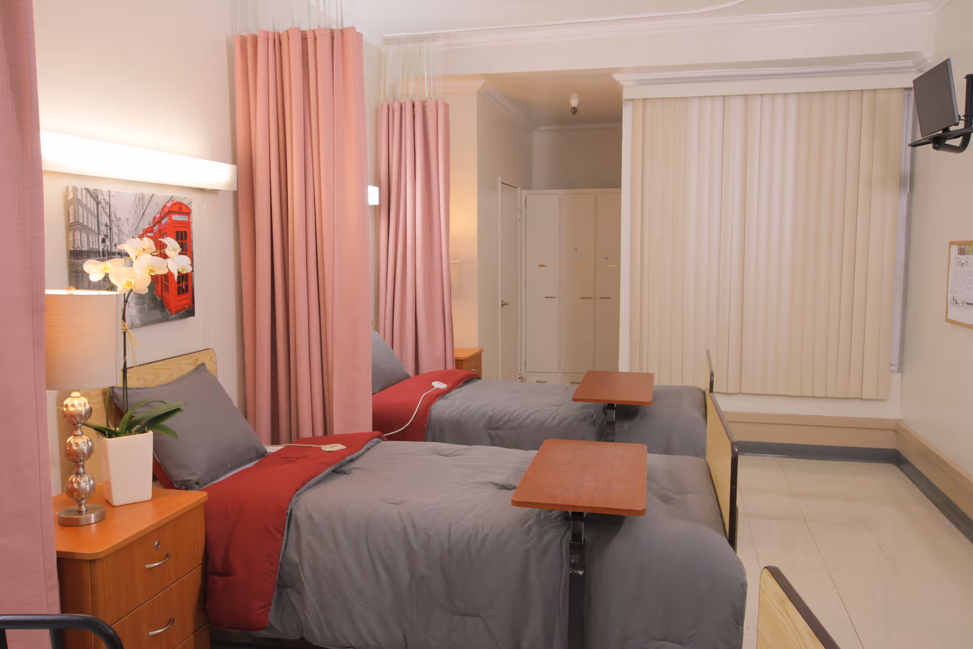 Two beds with pink curtains and bedside tables in a double-occupancy senior living bedroom.