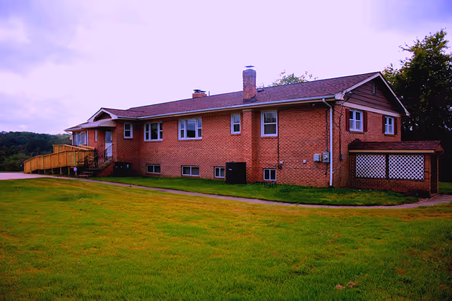 Single-story red brick building with multiple windows, a wheelchair ramp entrance and a large grassy lawn.