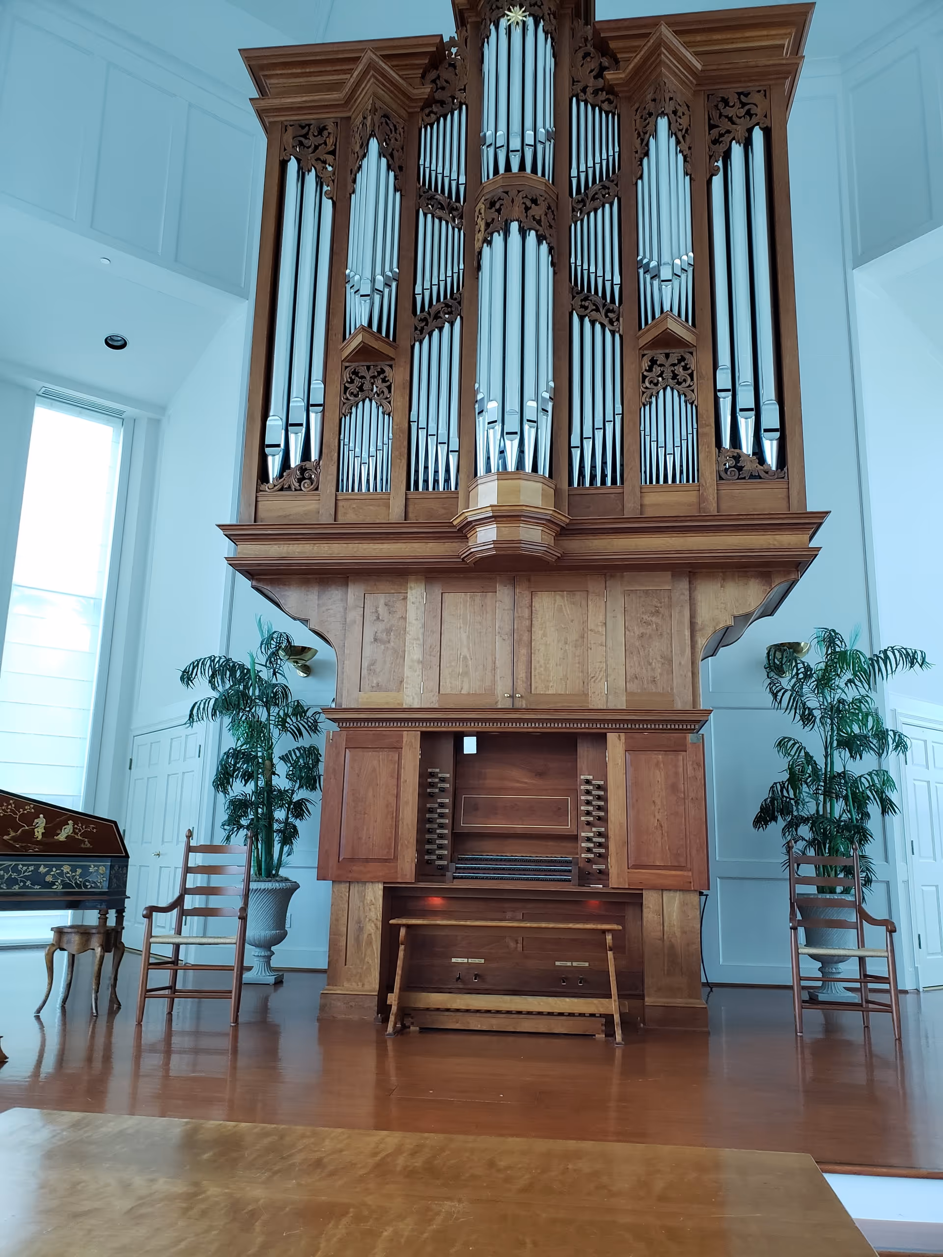 Inside Moorings Park, a large wooden pipe organ dominates a bright interior with chairs and plants.