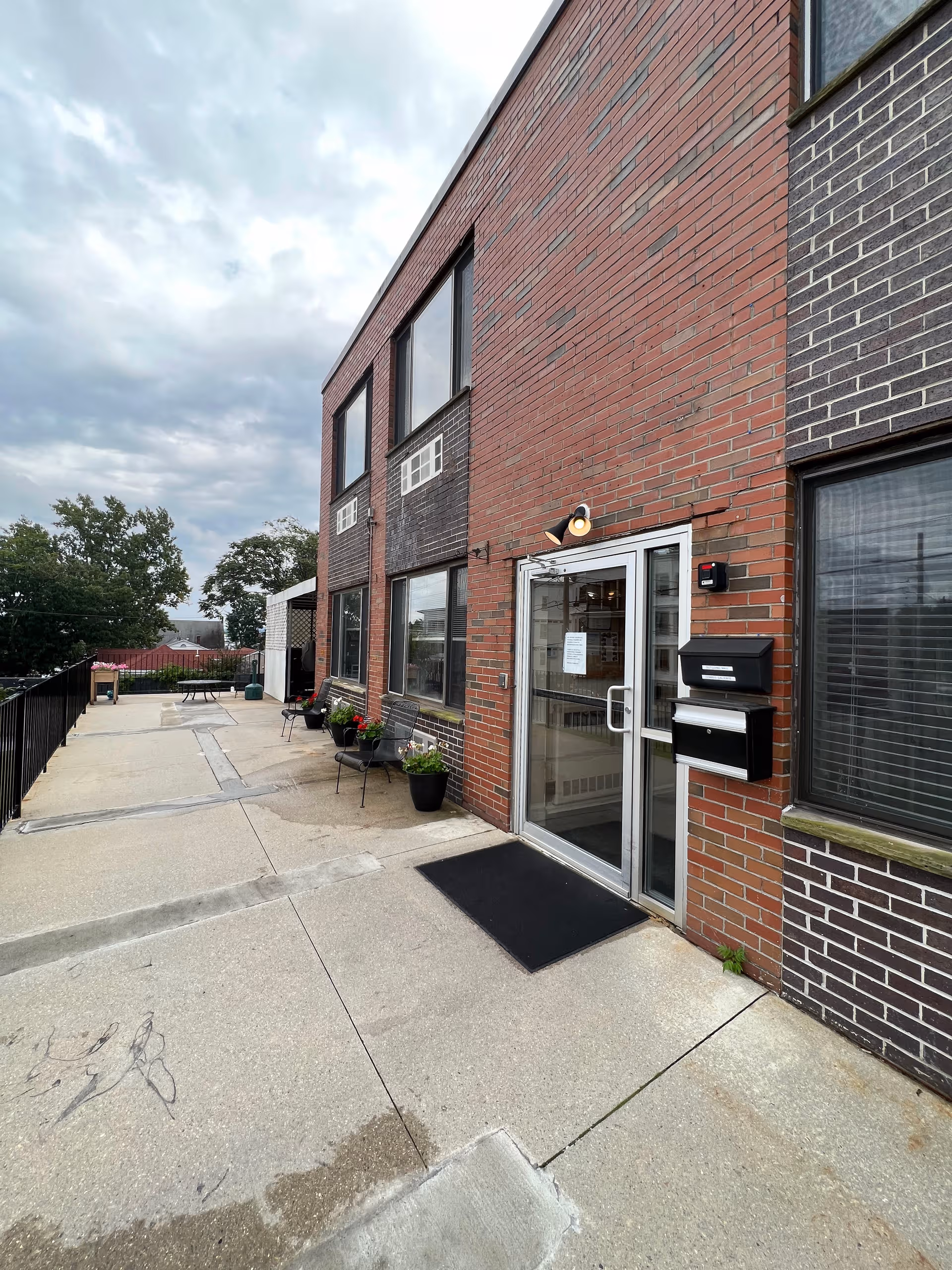 Brick senior living facility entrance with glass doors and outdoor seating along walkway.