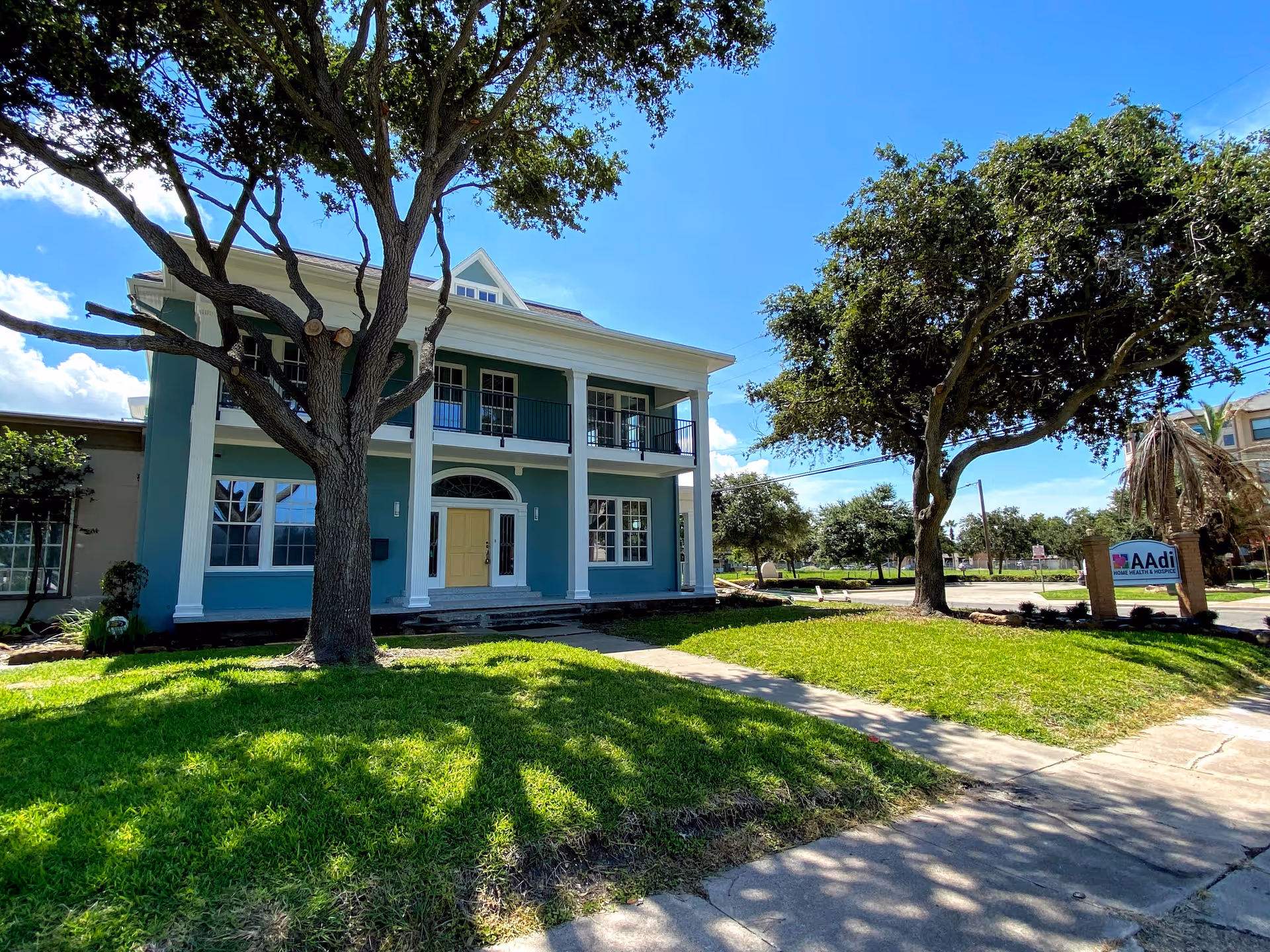 Blue two-story AAdi facility exterior with columns, lawn, and a sign by the driveway.