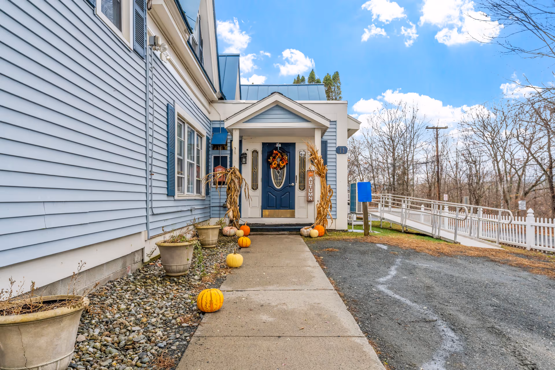 Blue senior living building entrance with pumpkins along a paved walkway.