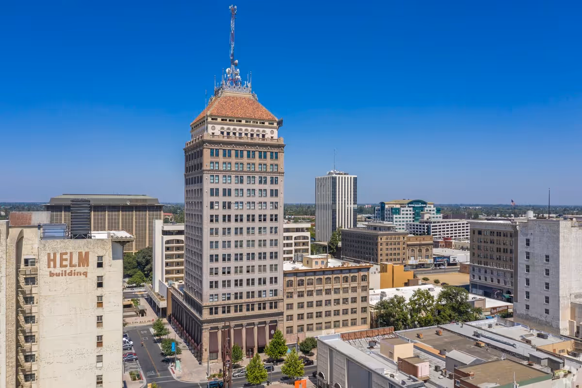 Aerial view of a downtown skyline with a tall central building under a clear blue sky.
