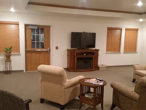 Cozy living room with beige chairs, fireplace mantle TV, and magazines on a side table.