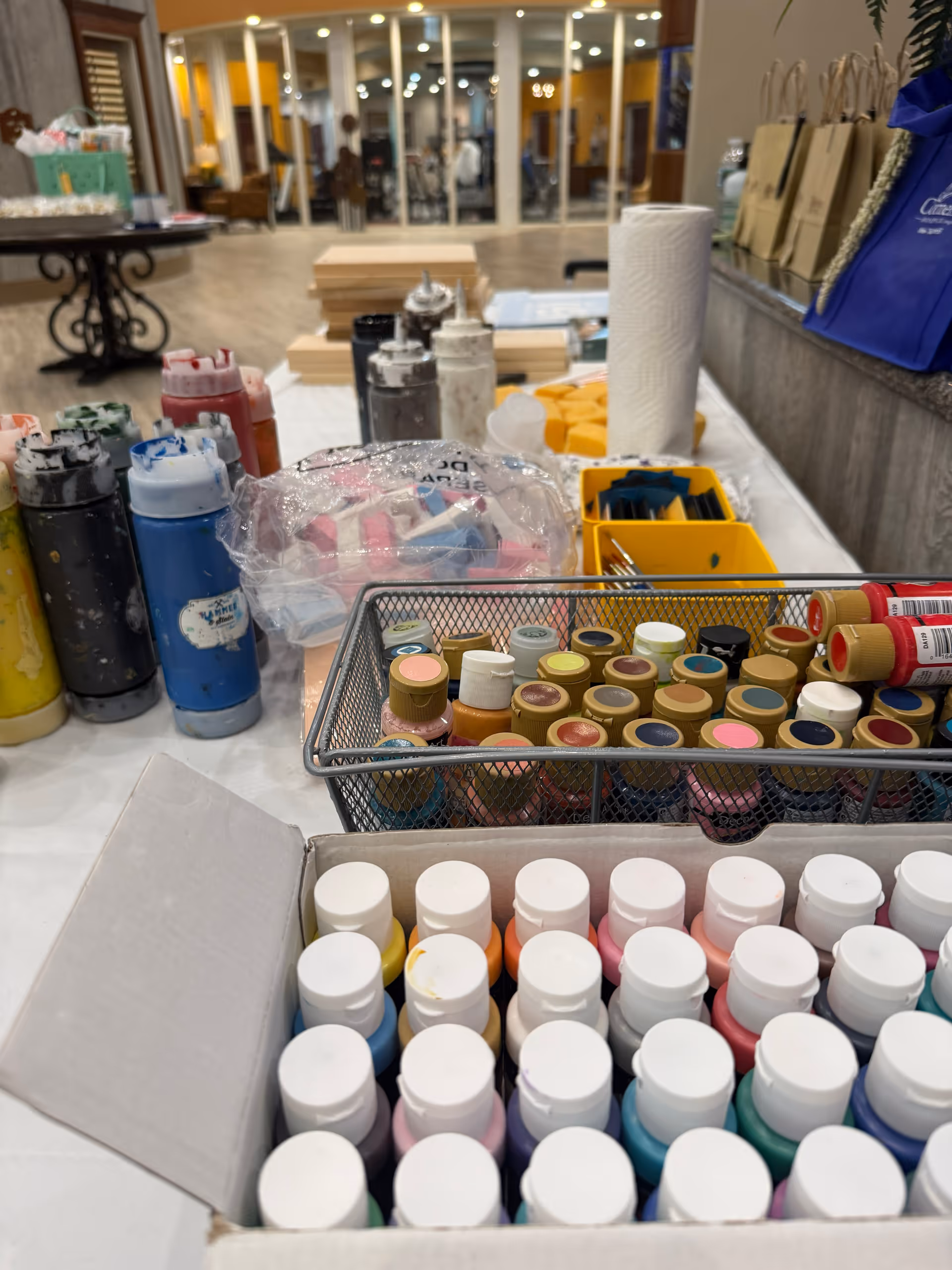 Art supplies, paints, and brushes arranged on a table inside a senior living facility lobby.