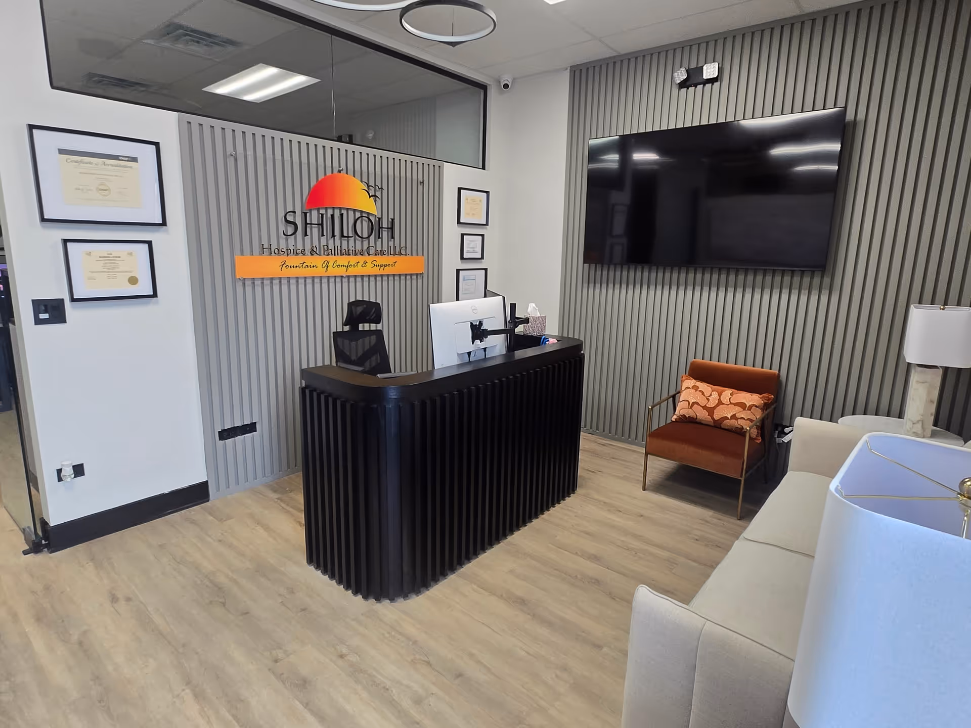 Reception area with a black curved desk and Shiloh Hospice sign on gray panel walls.