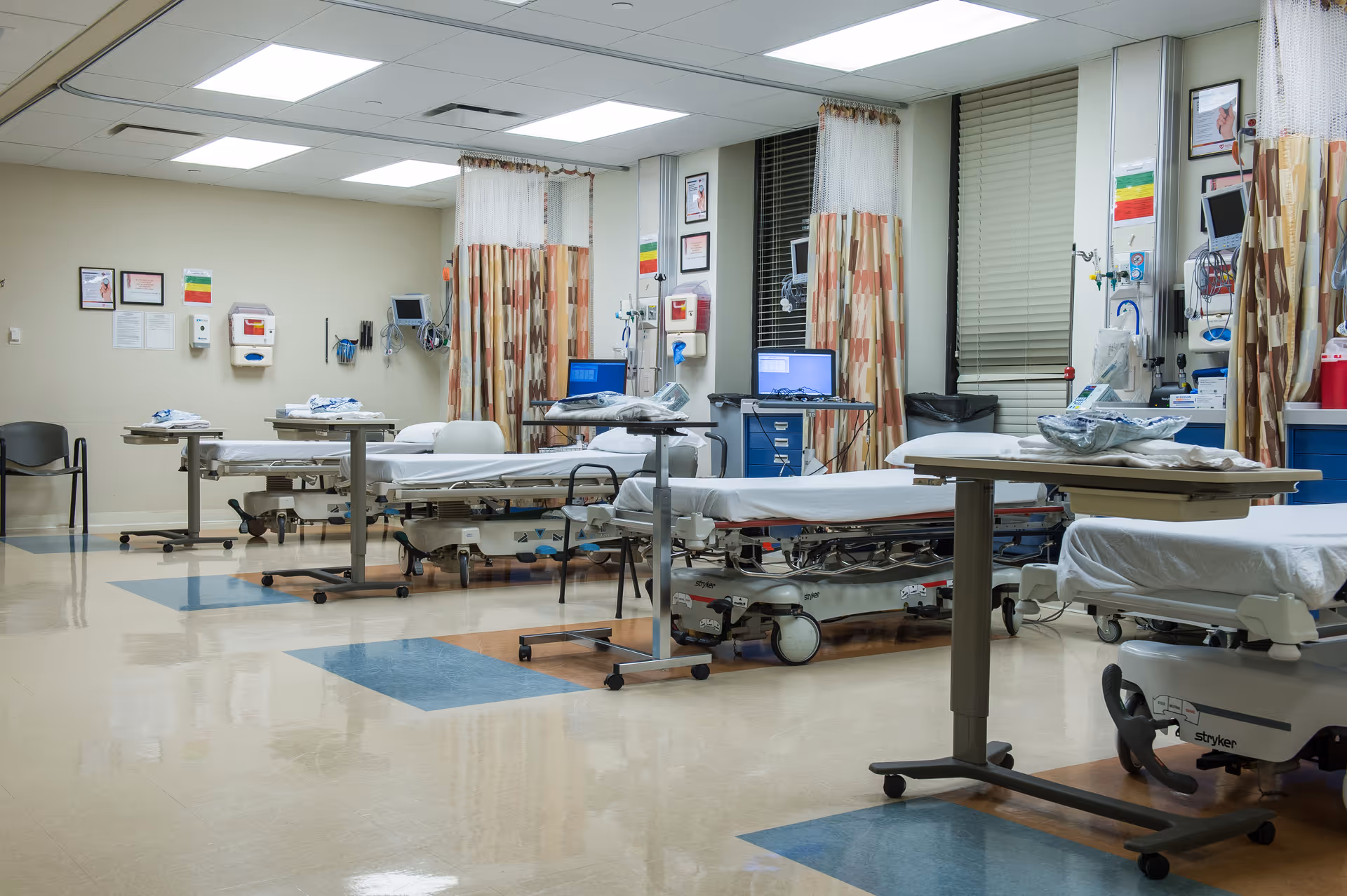 A medical ward with multiple hospital beds, curtains, monitors, and equipment.