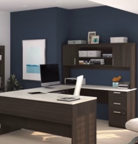 Modern office workspace with dark wood desk, computer, and wall-mounted shelves inside blue walls.