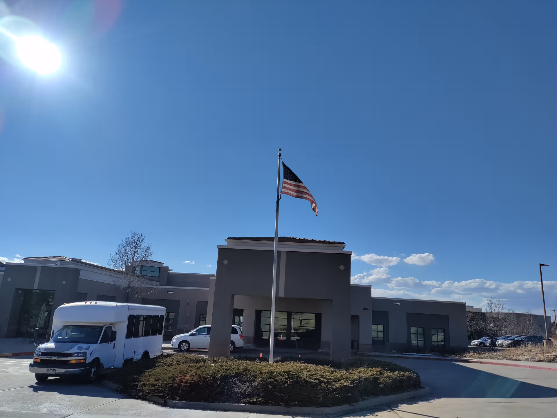 Exterior of a modern senior living facility with flagpole, van, and circular driveway.