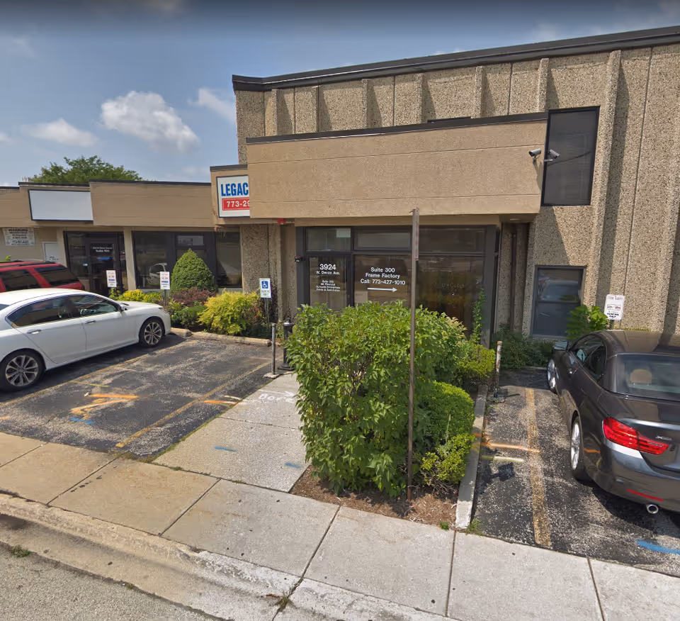 Exterior storefront with accessible parking, parked cars, and trimmed shrubs in front.
