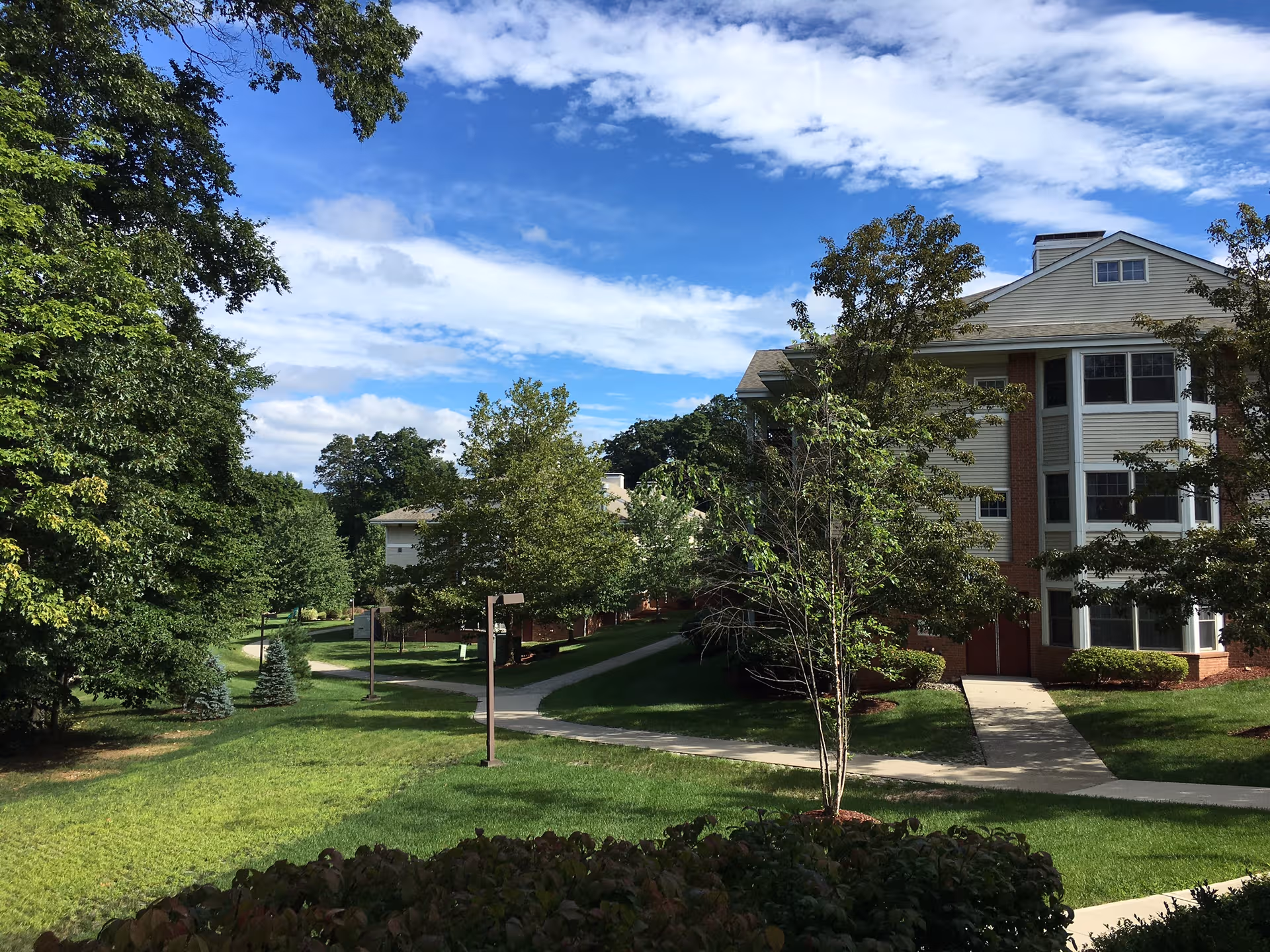 Exterior view of Fountainview senior living campus with trees, walkway, and a brick-and-siding building.