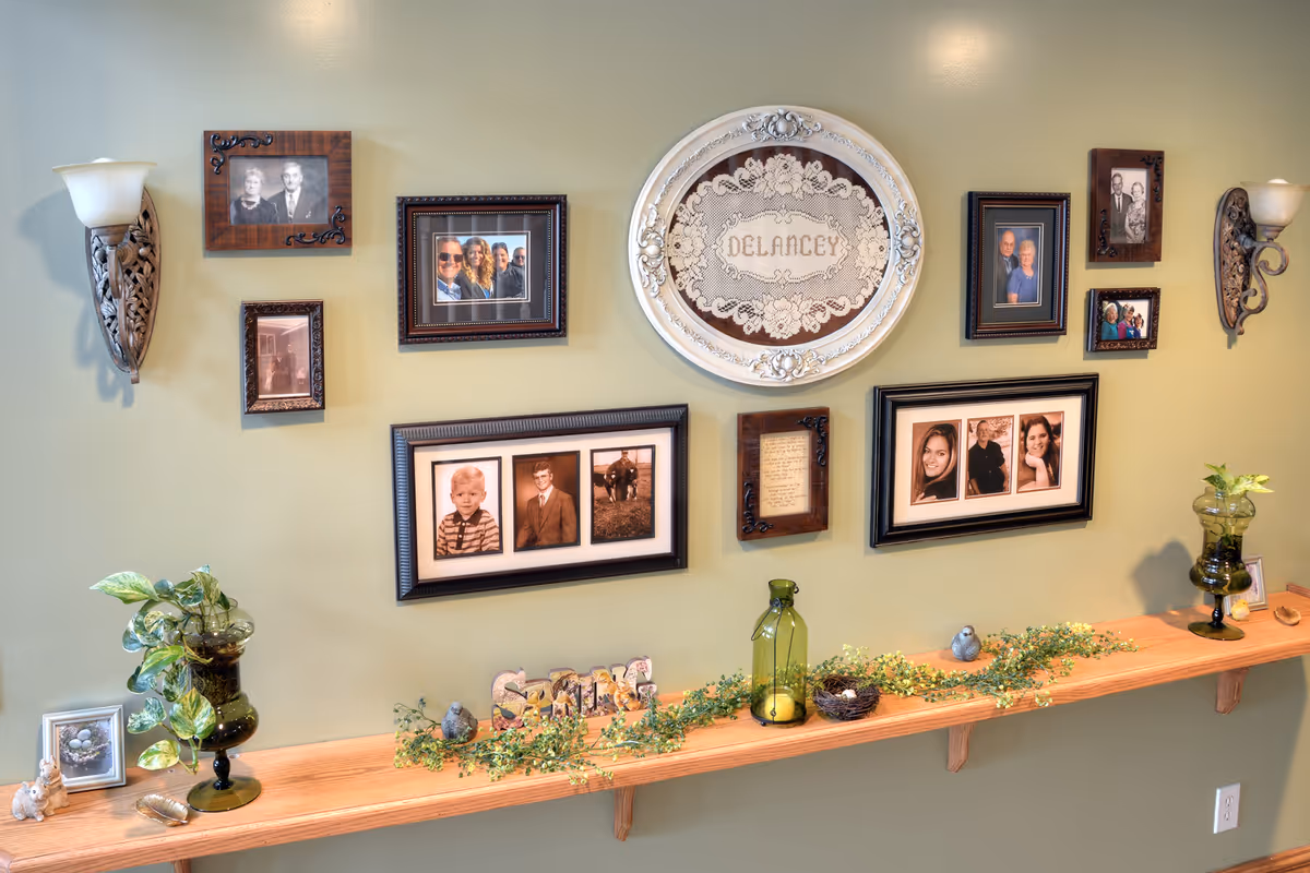 Decorative wall display of framed photos, a central circular plaque, and a wooden shelf with plants.