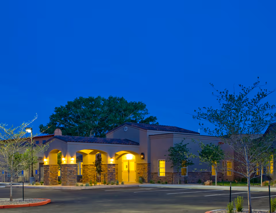 A senior living facility with arched entrances and warm exterior lighting at dusk.