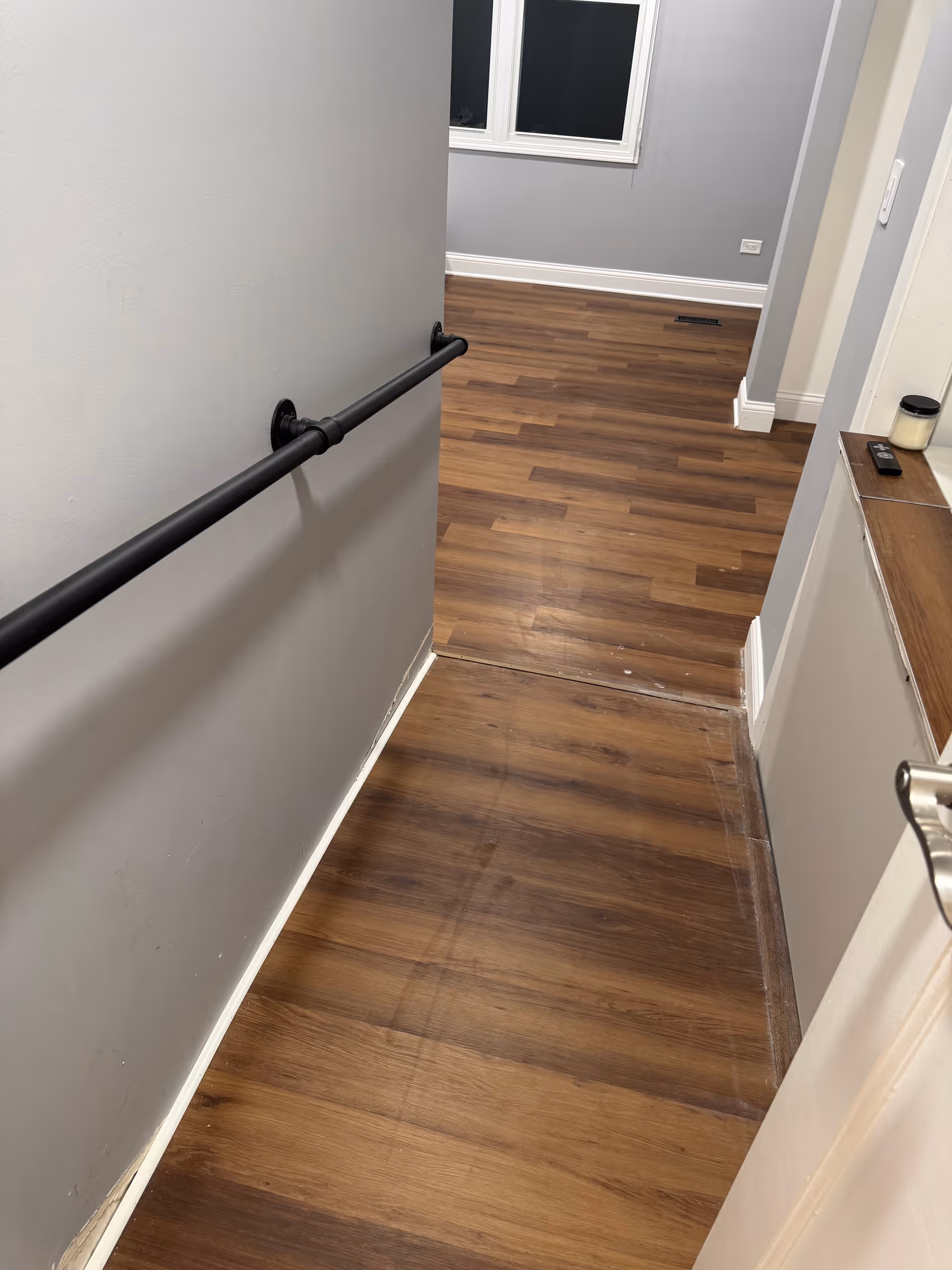 Interior hallway with wood floor, wall handrail, and a windowed room ahead.