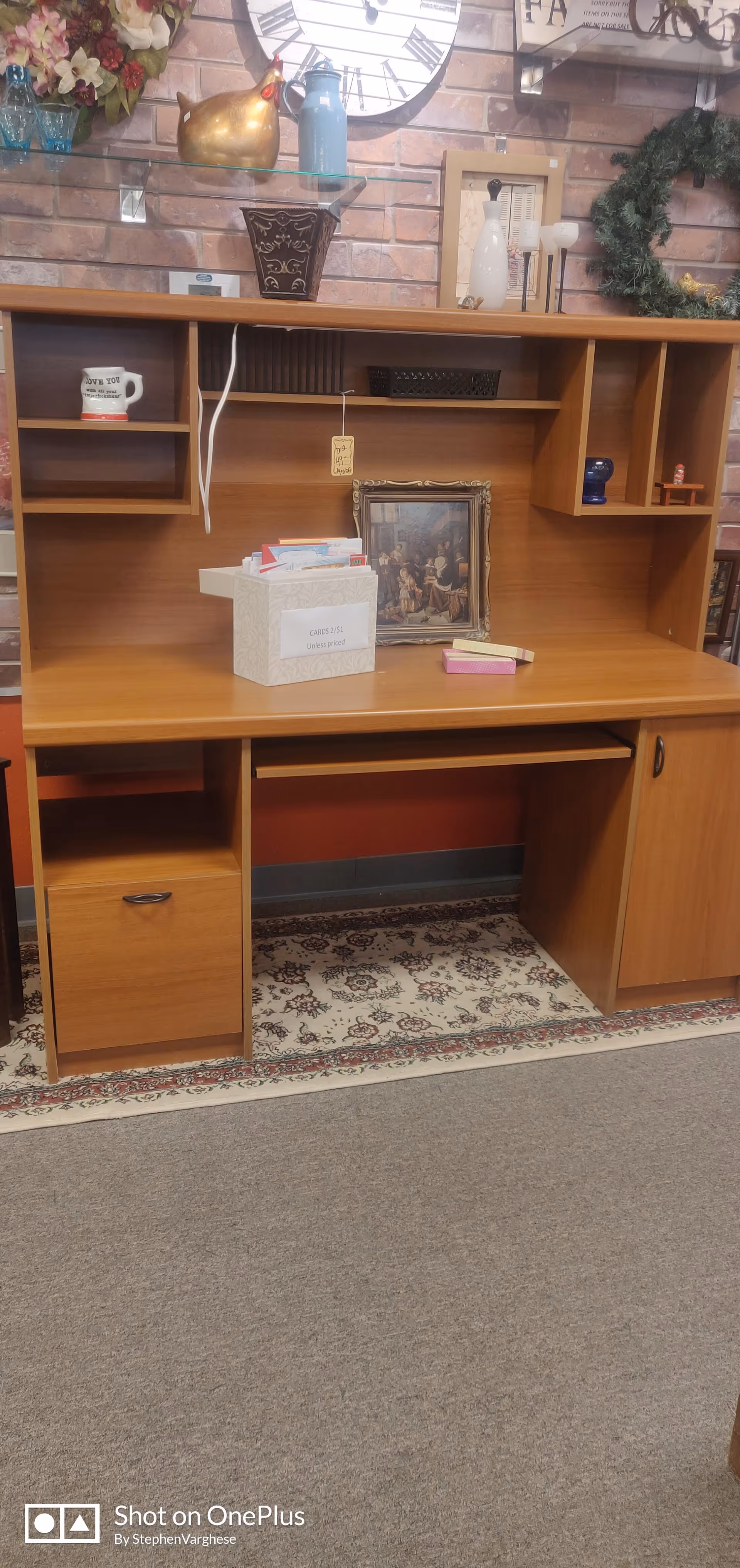Wooden desk with shelves against brick wall, cluttered with decor and a framed photo