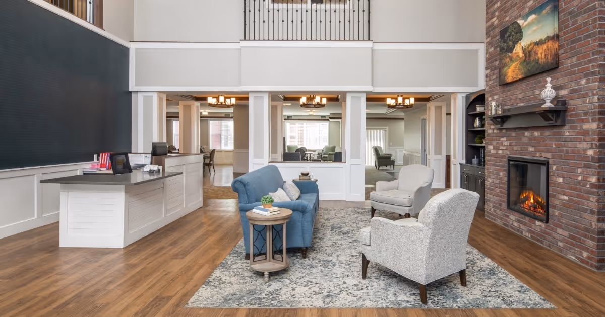 Spacious senior living common area featuring a fireplace, seating, and a reception desk.