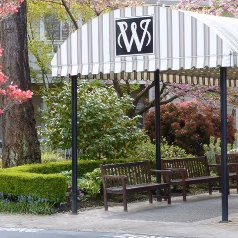 Entrance of Weatherly Inn Tacoma with a striped awning and benches in a landscaped area.
