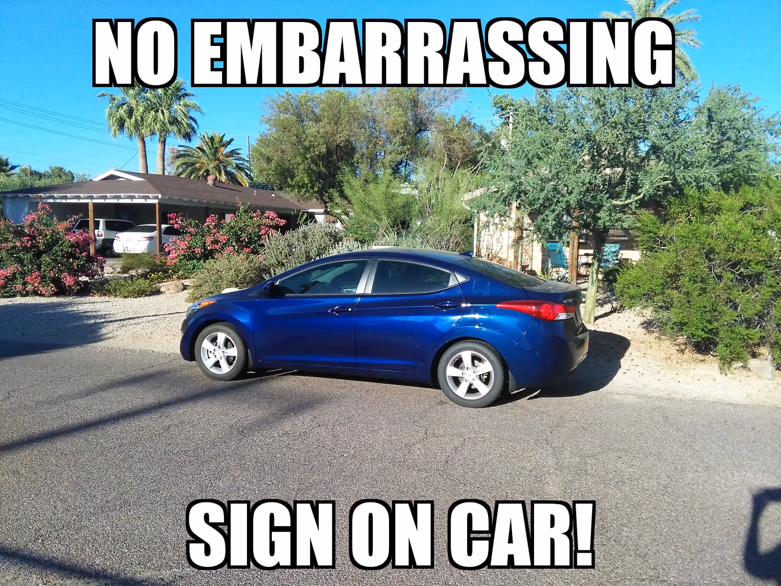 Blue sedan parked on a suburban street with a carport and shrubs