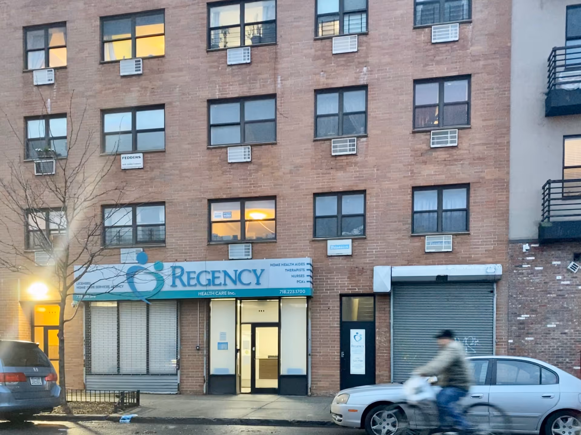 Brick building with Regency Health Care storefront and a cyclist passing by.