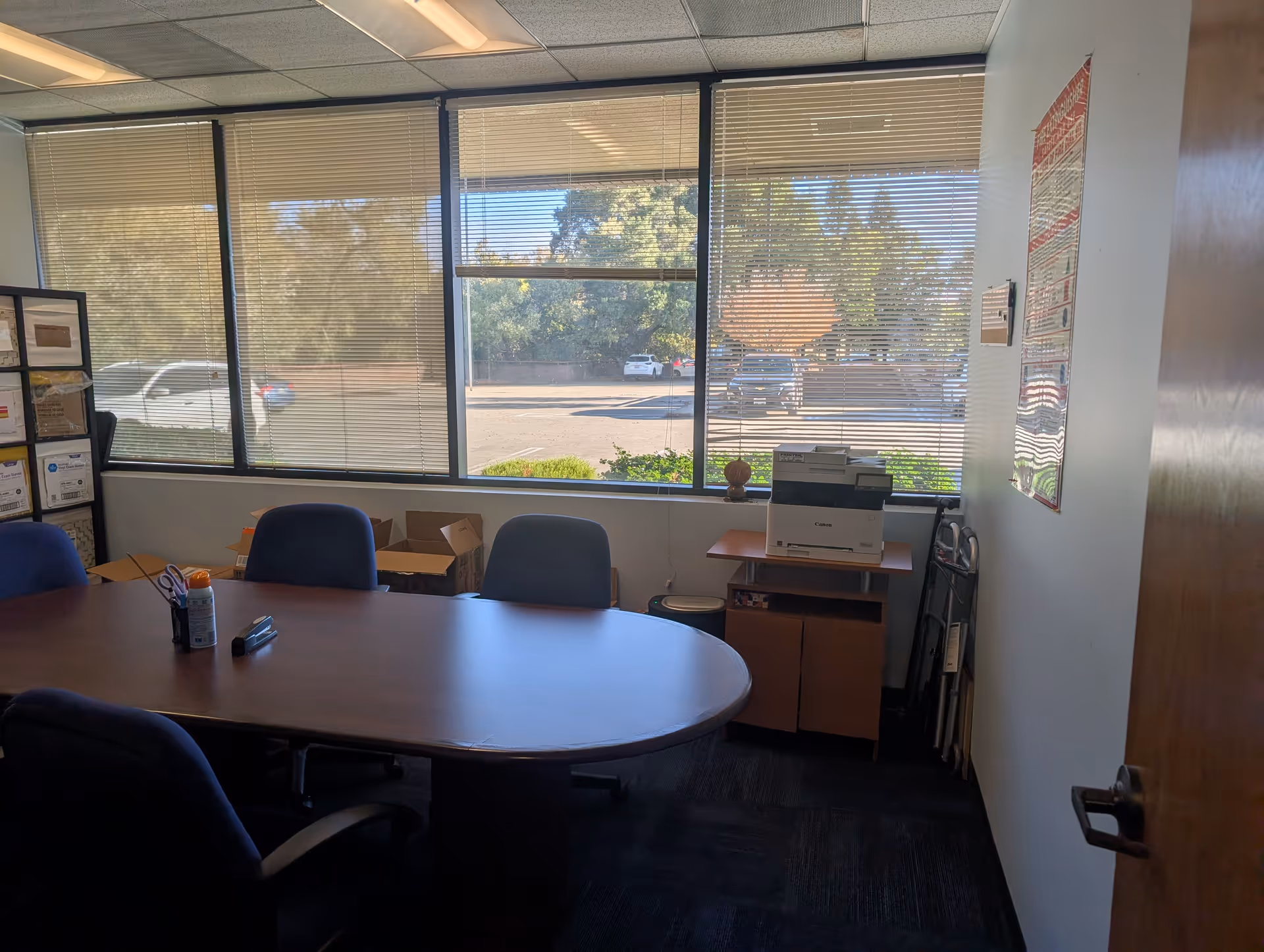 Office conference room with an oval table, blue chairs, and large windows.