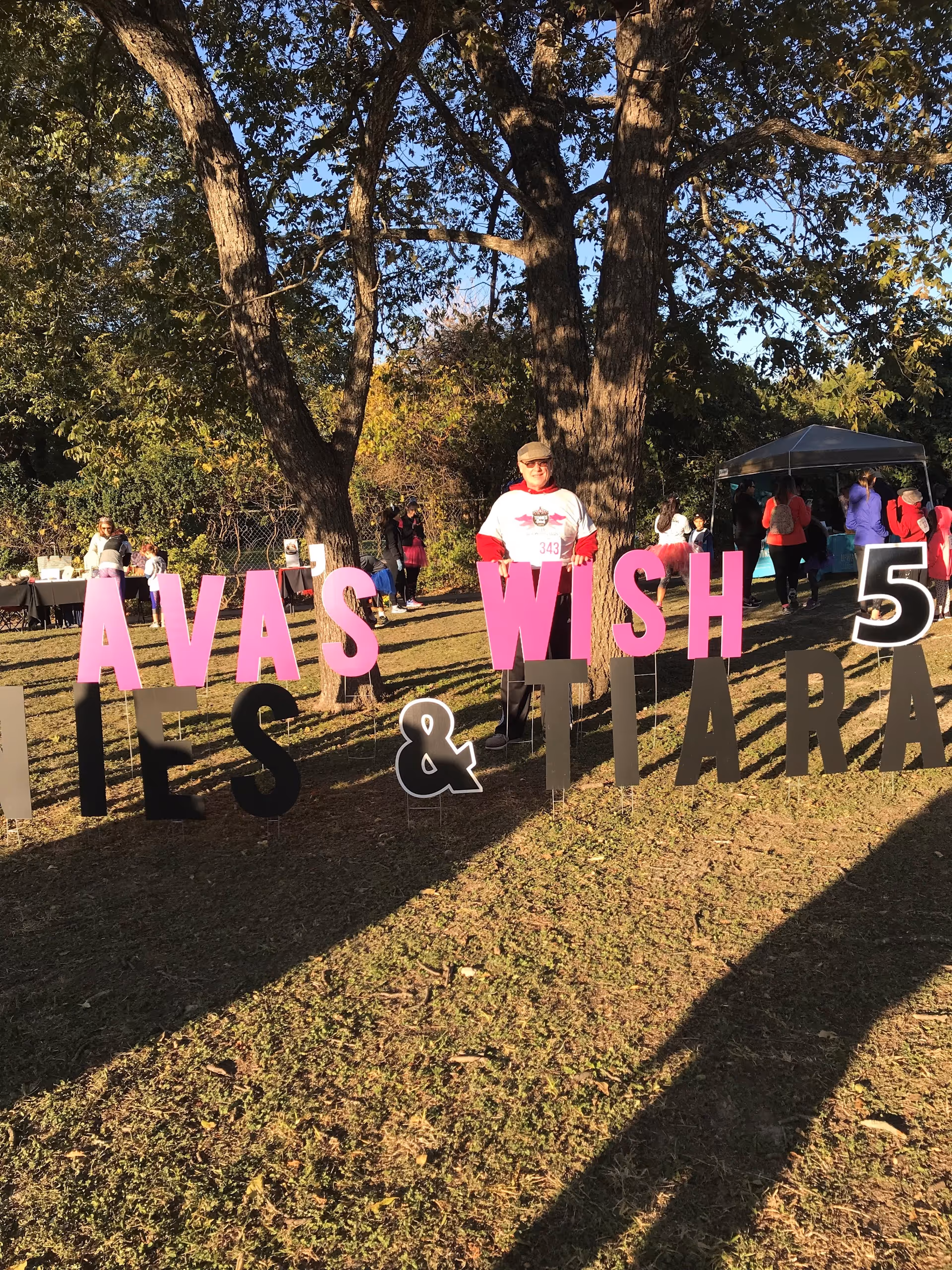People gather at an outdoor event with large pink letters and a tent in a park.