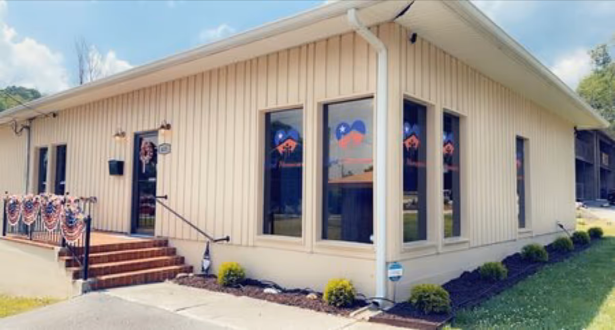 Cream-colored senior living facility with large windows, steps, and patriotic bunting at the entrance.
