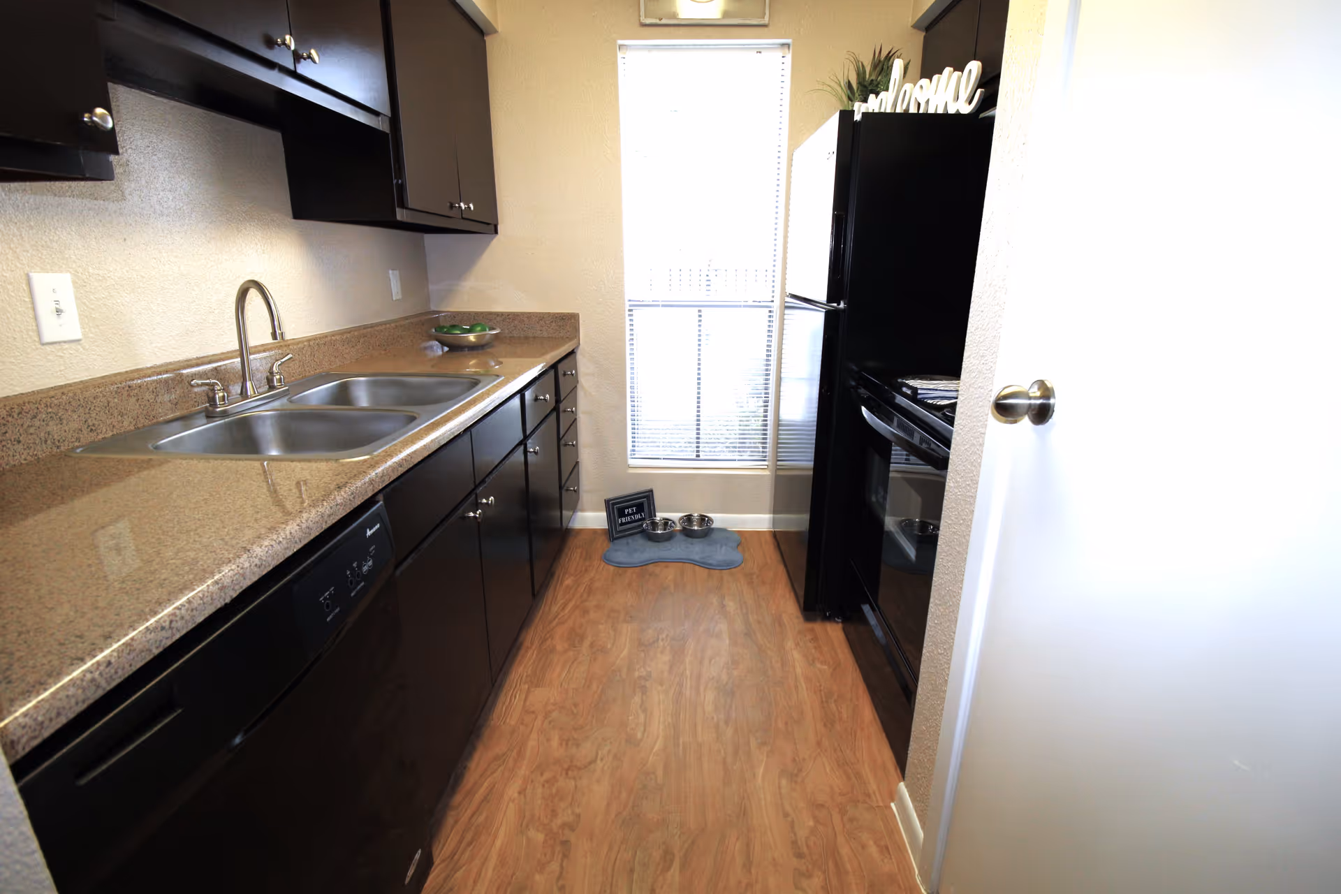 Narrow galley kitchen with black cabinets, granite counters, and stainless appliances.