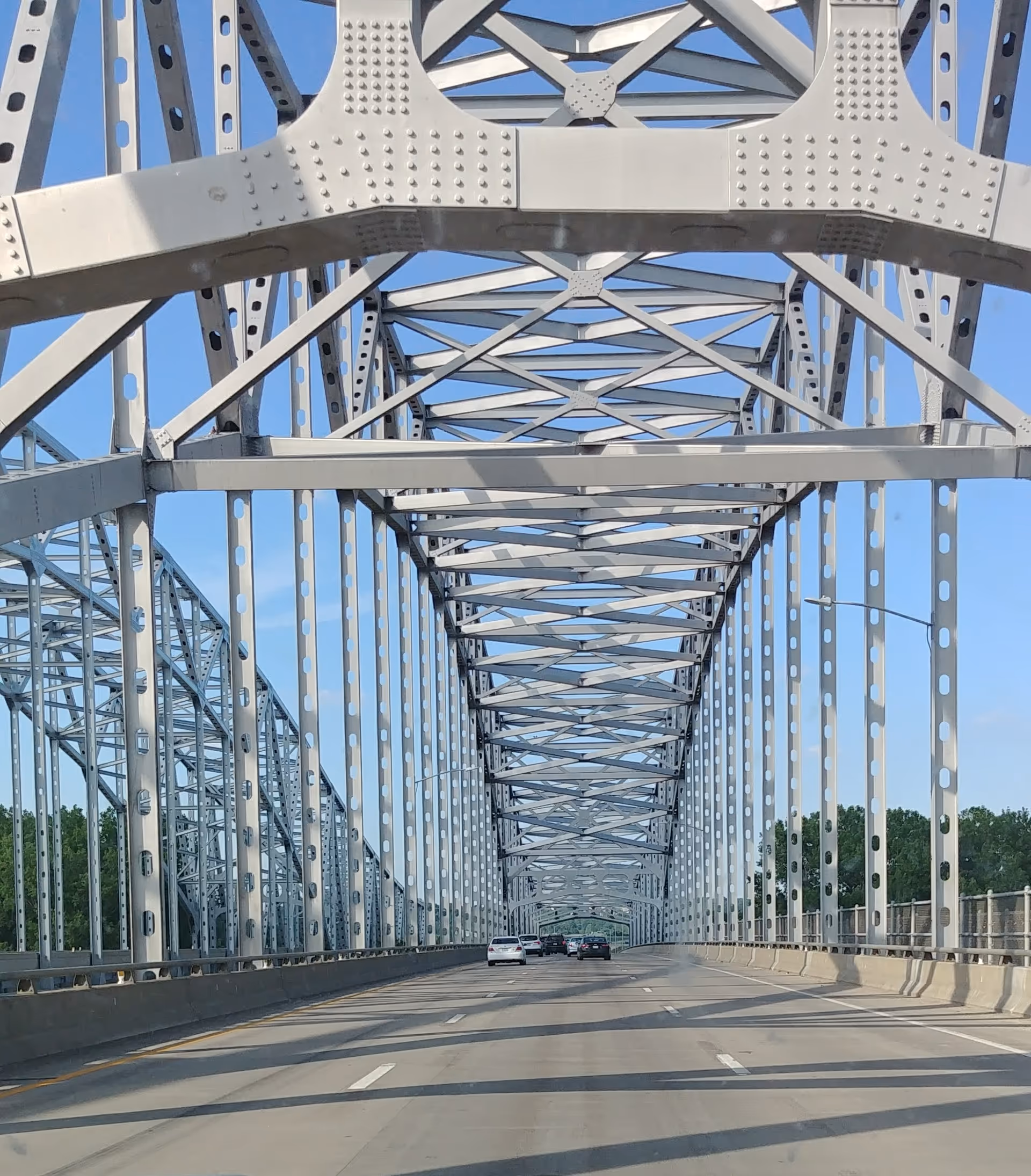 A metal truss bridge with vehicles driving along a sunlit roadway