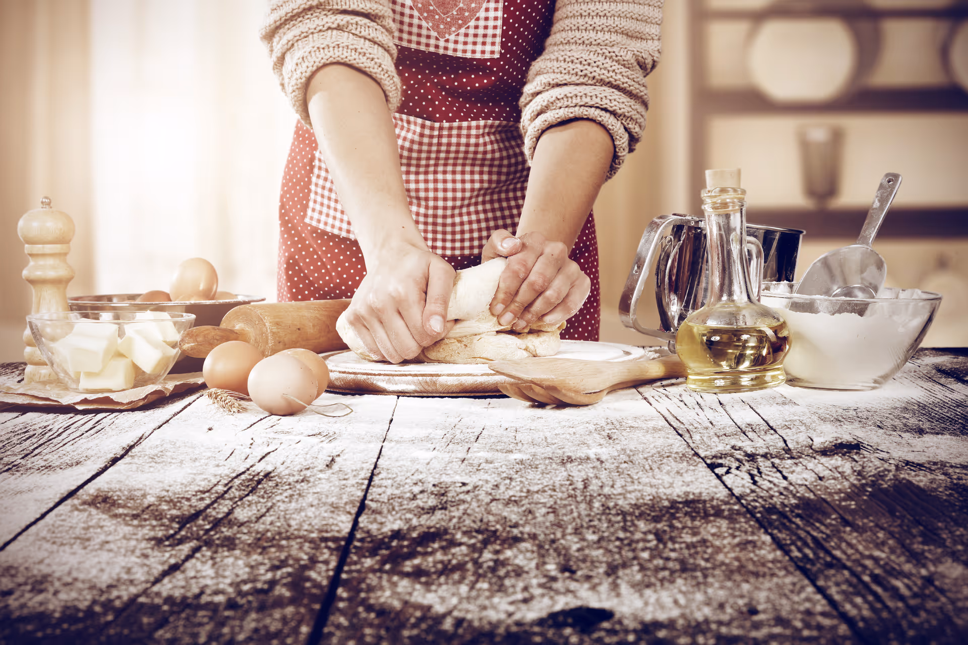 A person kneads dough on a rustic kitchen counter with eggs, oil, and bowls.