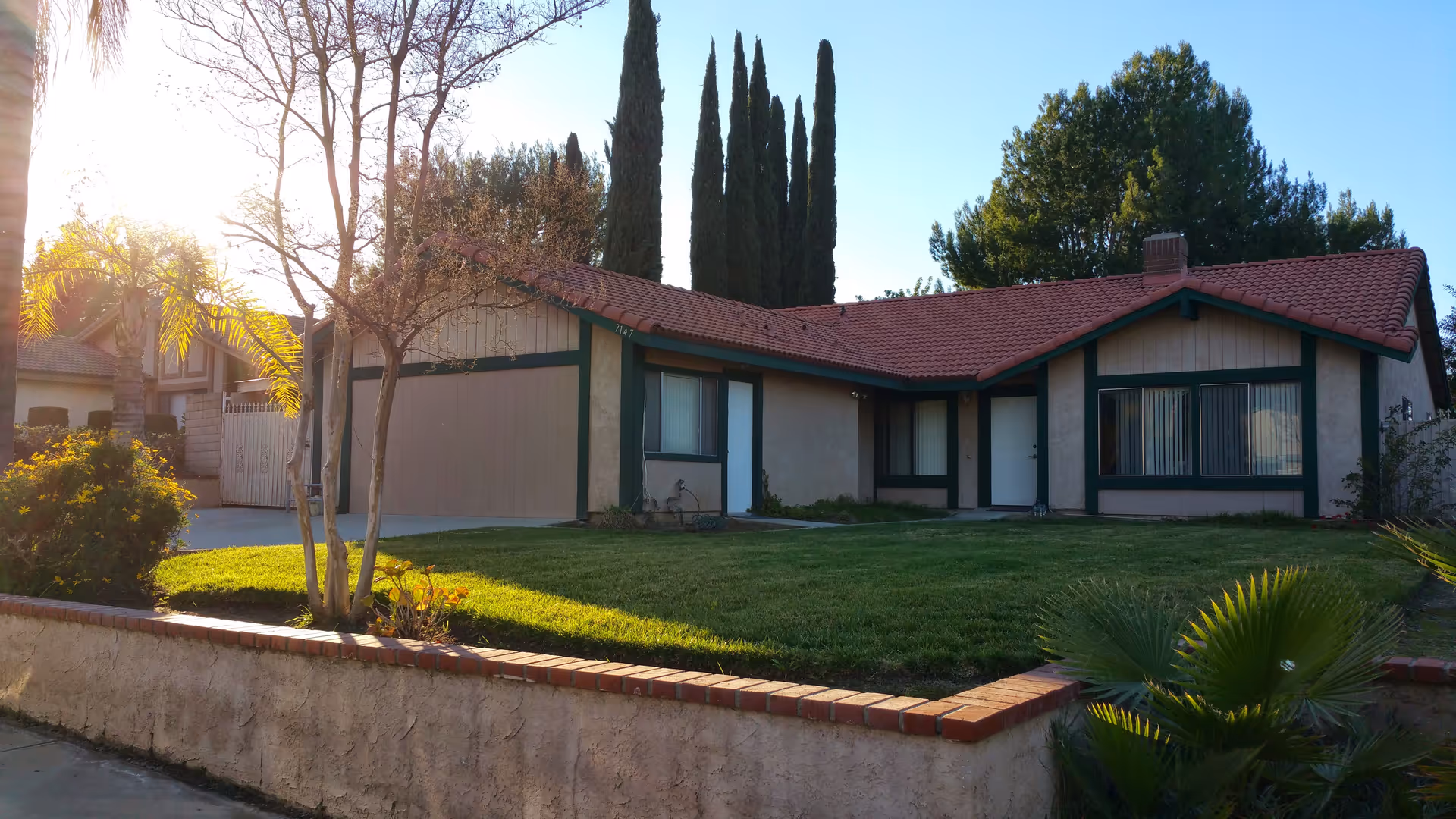 Single-story beige building with a red-tiled roof, front yard, and palm trees.