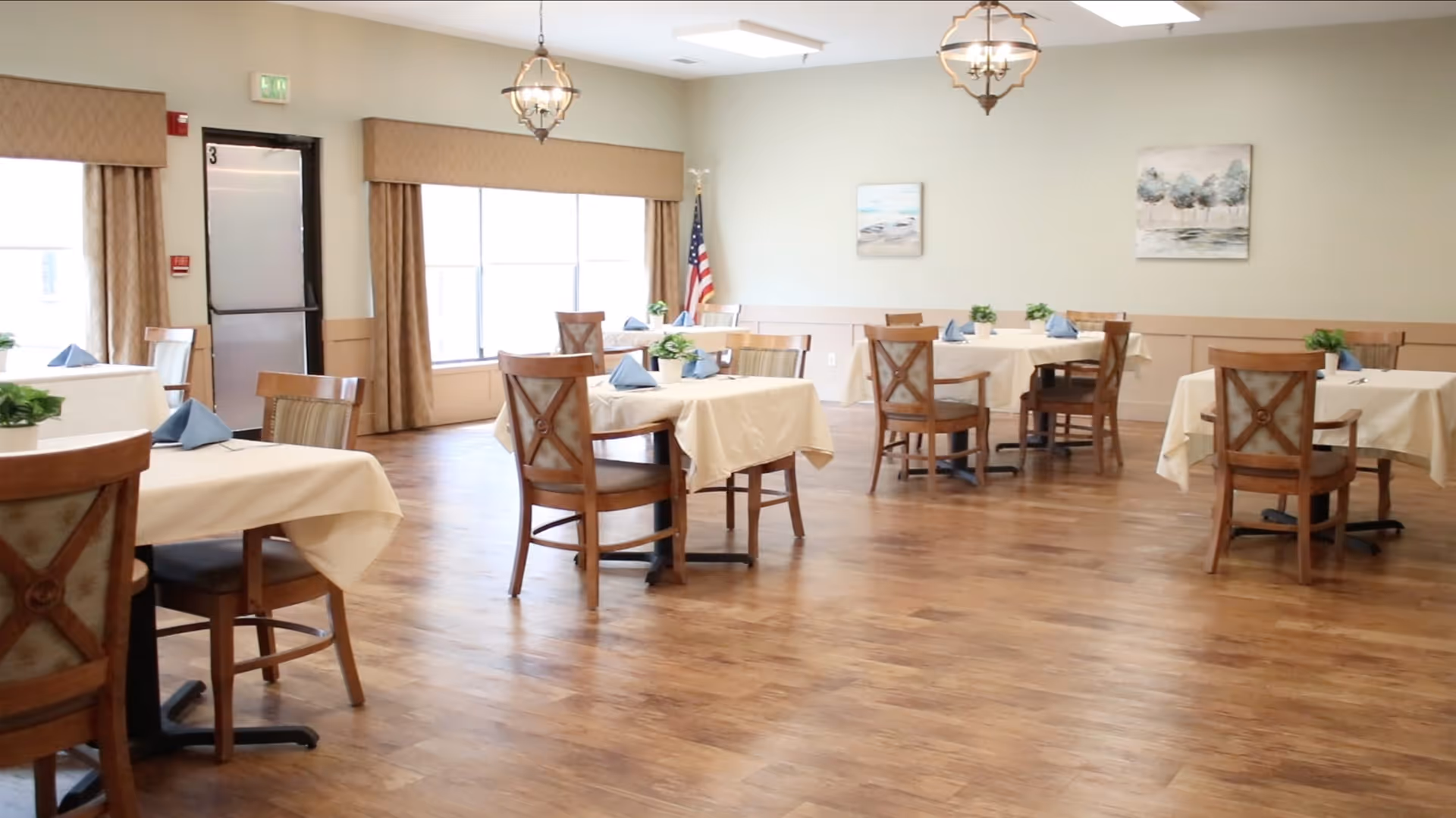 A spacious senior living dining room with multiple tables set with white tablecloths.