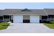 Front view of a single-story residential building with two garage doors and a wide driveway.