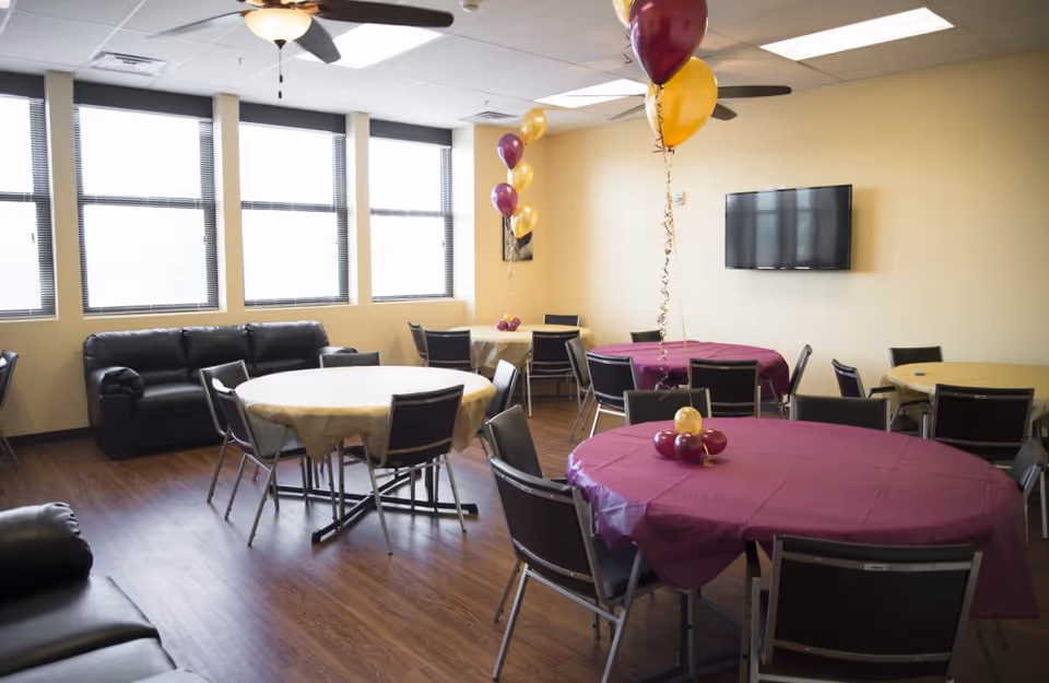 Bethlehem Manor common room with round tables, balloons, and a wall-mounted TV.