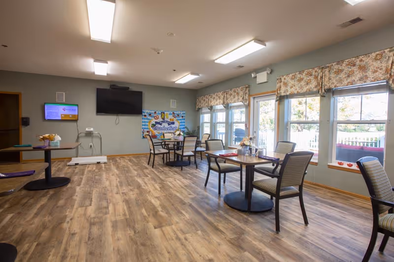 Bright communal dining area at Sunset Ridge Assisted Living with tables, chairs, and large windows.