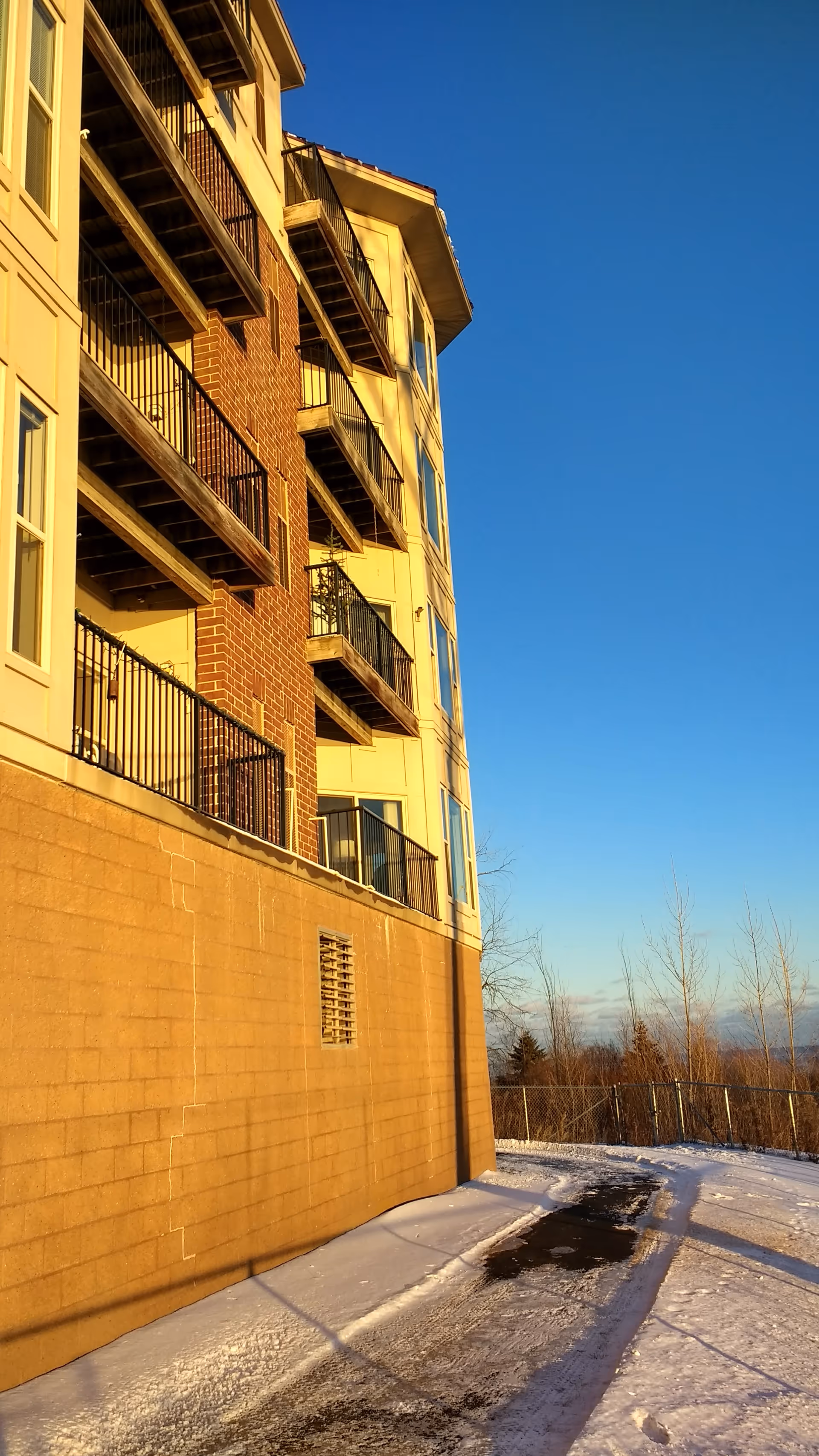 Exterior view of a multi-story residential building with balconies, brick and beige siding, snow-covered ground.
