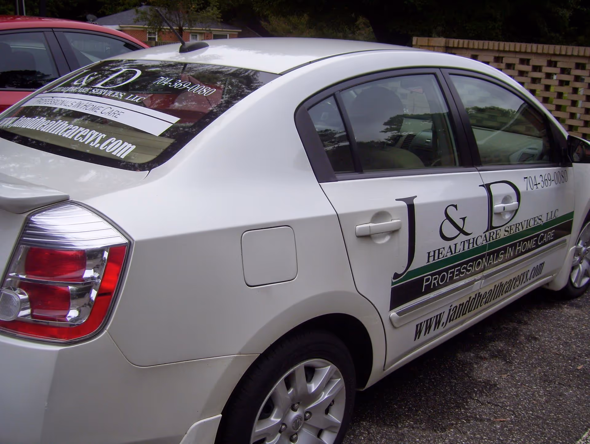 White sedan with J & D Healthcare Services branding parked outdoors.