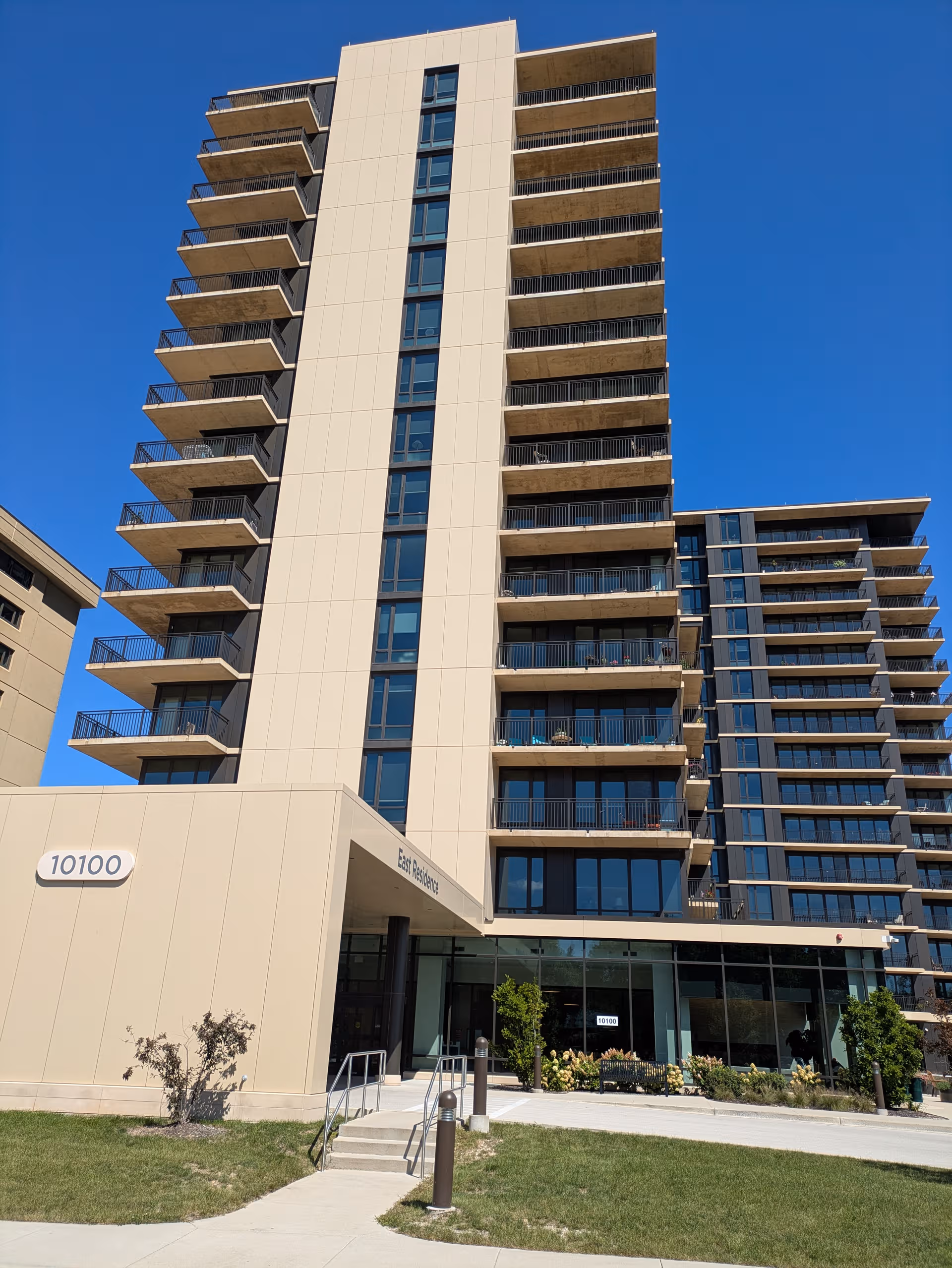 Tall modern senior living building with many balconies and a glass entrance.