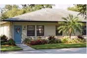 Single-story senior living building with a blue front door, palm tree, and landscaped yard