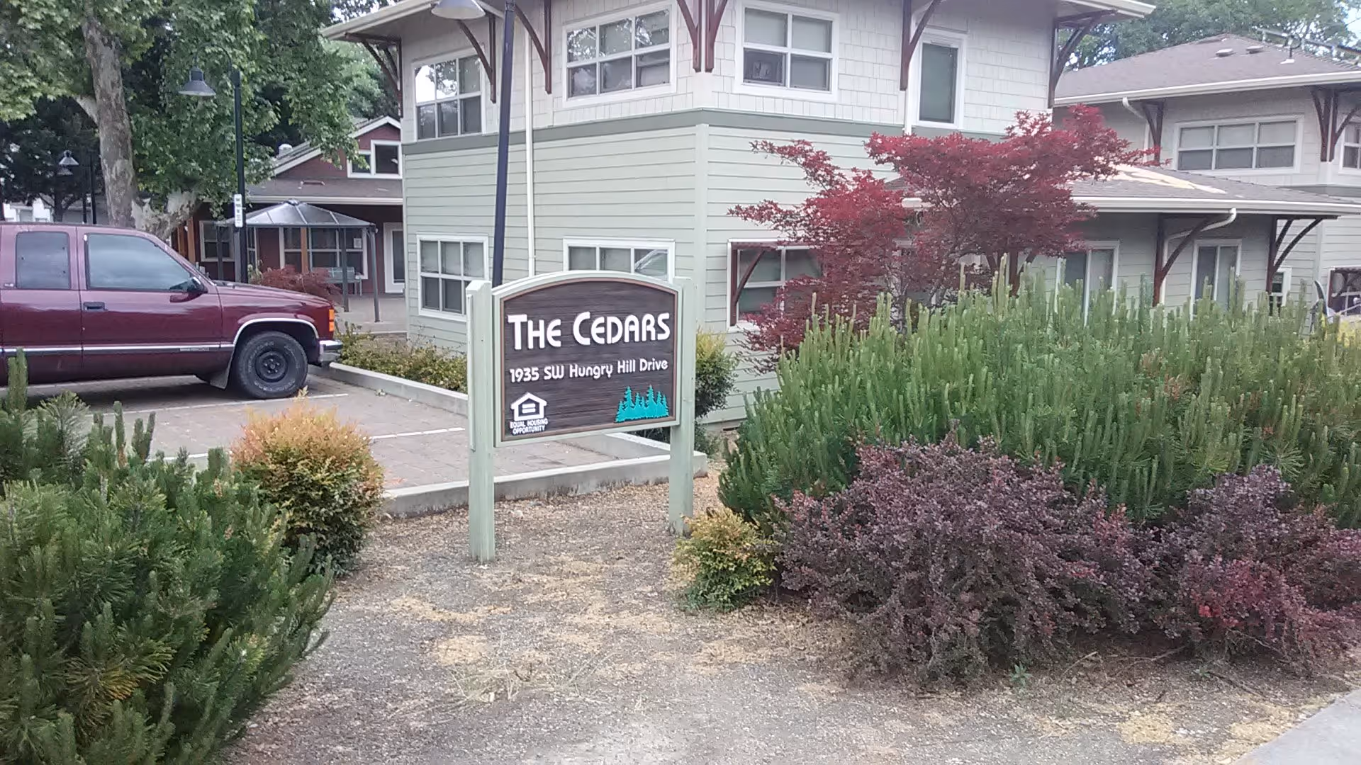 Exterior view of The Cedars senior living facility with a sign and landscaping.