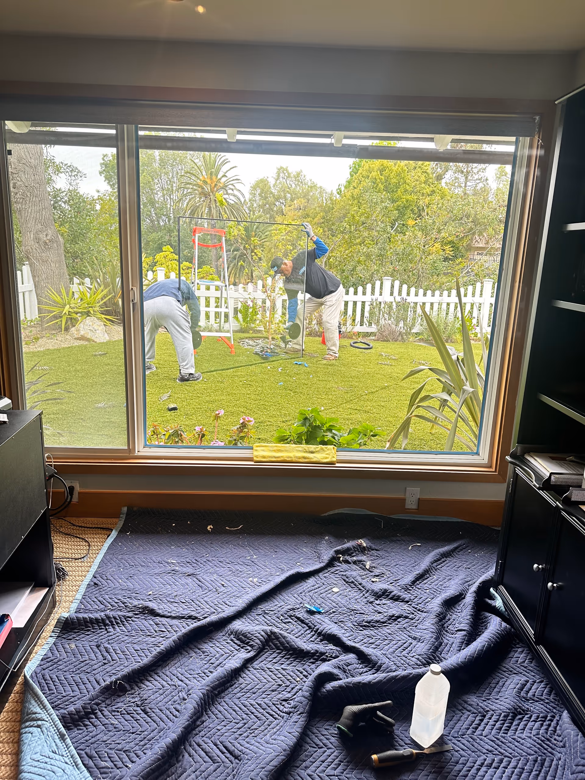 Inside room with a large window showing two people outside using gym equipment in the yard.