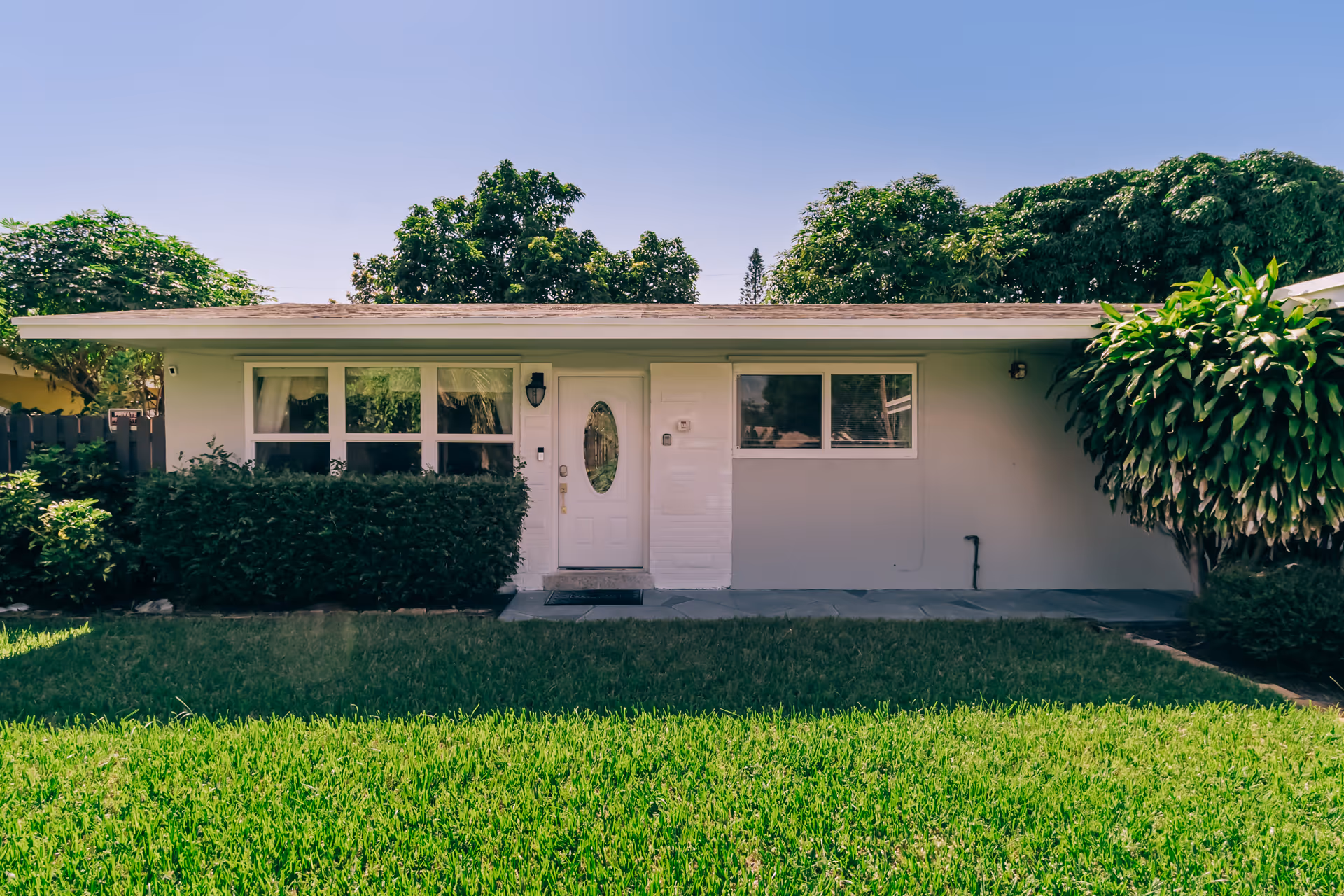 Front exterior of a single-story building with a white door, large windows, and a green lawn.