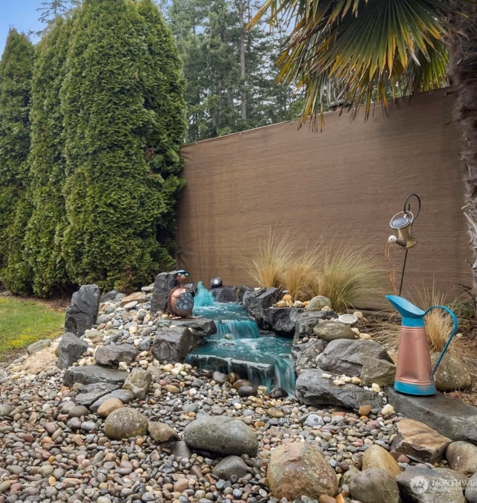 Outdoor rock garden with a small waterfall, pebbles, and garden decorations.
