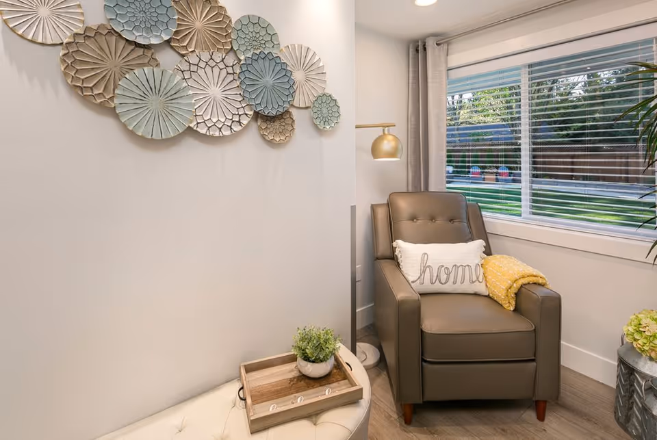 Cozy living room corner with armchair, wall art, plant, and window view.